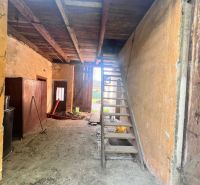 Sklad v rodinném domě s dřevěným schodištěm a hliněnou podlahou.