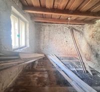 Pokoj v rodinném domě s kamennými stěnami a dřevěným stropem, materiál na podlaze.