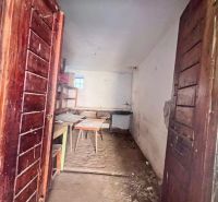 Dřevěné dveře vedou do místnosti rodinného domu s nábytkem a surovou podlahou.