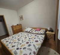 Ložnice v 3pokojovém bytě s postelí, komodou a podlahou s dřevěným dekorem.