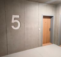 Betonová stěna s číslem pět a dřevěnými dveřmi v 2-pokojovém bytě.