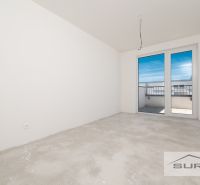 Prázdný pokoj v 3-pokojovém bytě se vstupem na balkon a nedokončenou podlahou.
