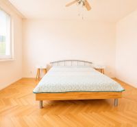 Světlá ložnice s podlahou s dřevěným dekorem a dvoulůžkem v 2-pokojovém bytě.