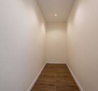 Úzká chodba v rodinném domě s bílými stěnami a podlahou s dřevěným dekorem.