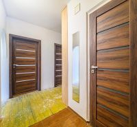 Chodba v 3-pokojovém bytě s dřevěnými dveřmi a podlahou s dřevěným dekorem.