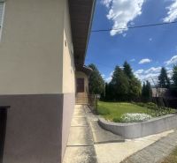 Rodinný dům v Orlové s chodníkem a zelení, obklopený stromy a modrou oblohou.
