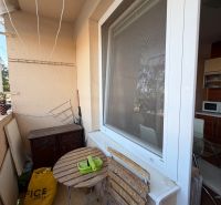 Balkon 3pokojového bytu s dřevěným stolem a židlemi, vedle kuchyňského okna.