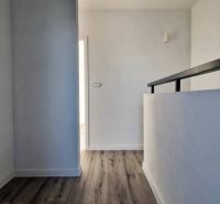 Chodba v rodinném domě s podlahou s dřevěným dekorem a bílými stěnami.