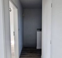 Chodba v rodinném domě s bílými stěnami a podlahou s dřevěným dekorem.