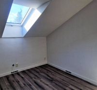 Podkrovní pokoj s velkým střešním oknem a podlahou s dřevěným dekorem v rodinném domě.