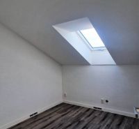 Podkrovní pokoj s podlahou s dřevěným dekorem a střešním oknem v rodinném domě.