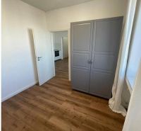 Pokoj v 3-pokojovém bytě s podlahou s dřevěným dekorem, šedou skříní a oknem.