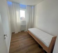 Úzký pokoj s postelí a podlahou s dřevěným dekorem ve 3pokojovém bytě.