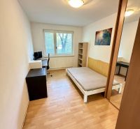 Pokoj ve 4pokojovém bytě s postelí, pracovním stolem a podlahou s dřevěným dekorem.
