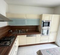 Kuchyně ve 4-pokojovém bytě s bílými dlaždicemi a linkou s dřevěným dekorem.