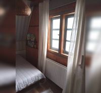 Pokoj v rodinném domě s tmavým dřevěným obkladem a postelí u okna.