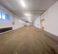 Interiér skladu s betonovou podlahou a bílými stěnami, zářivkové osvětlení.