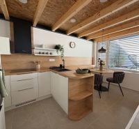 Kuchyně v rodinném domě s podlahou s dřevěným dekorem, dřevěnými trámy a jídelním stolem.