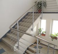 Schodiště v kanceláři s nerezovým zábradlím, květinami a velkými okny.