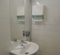 Umyvadlo v kancelářích s dávkovačem mýdla a zrcadlem na stěně.