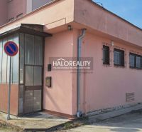 Exteriér budovy kanceláří v Senci se zákazovou značkou parkování a plechovými dveřmi.
