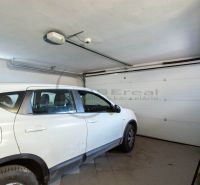 Auto zaparkované v garáži rodinného domu s bílými stěnami a podlahou z dlaždic.