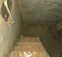 Schodiště vedoucí do sklepa se stěnami s viditelnými trubkami v Zahradách.