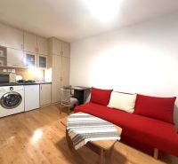 Rekreační apartmán s červenou sedačkou, kuchyňským koutem a podlahou s dřevěným dekorem.