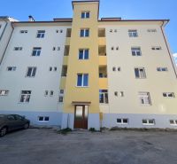 Bytovka v Banské Bystrici s parkovištěm před vchodem.