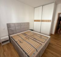 Ložnice s postelí, skříní a podlahou s dřevěným dekorem v 2-pokojovém bytě.