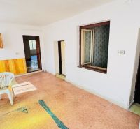 Interiér rodinného domu s plastovou židlí, dveřmi a elektrickou skříňkou na stěně.