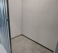 Malé skladové prostory s kovovými dveřmi a betonovou podlahou v 2-pokojovém bytě.