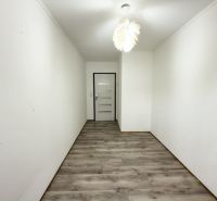 Úzká chodba v rodinném domě s podlahou s dřevěným dekorem a bílým stropem.