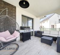 Terasa rodinného domu s pohodlným ratanovým posezením a grilem na podlaze s dřevěným dekorem.