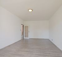Prostorná místnost s podlahou s dřevěným dekorem v 3-pokojovém bytě, bílé stěny.