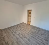 Pokoj se světlými stěnami a podlahou s dřevěným dekorem ve 4-pokojovém bytě.