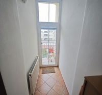 Úzká chodba s oknem a radiátorem v 2-pokojovém bytě, dlažba na podlaze.