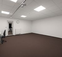 Priestranné kanceláře s bílými stěnami, hnědým kobercem a minimalistickým zařízením.