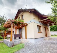 Chata v Moči má terasu s dřevěnou pergolou a zelení na ulici Moča.