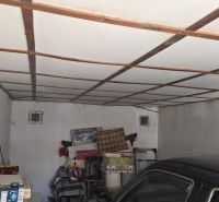 Garáže s bílým ventilátorem, uskladněnými věcmi a zaparkovaným autem.
