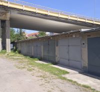 Garáže na Jesenského ulici ve Zvolenu pod mostem, obklopené zelení a štěrkovou cestou.