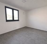 Prázdný pokoj s dlažbou, bílými stěnami a velkým oknem v rodinném domě.