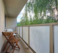 Balkon 2-pokojového bytu se skládacími židlemi a stolem, výhled na zeleň.