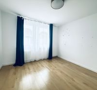 Světlá místnost s podlahou s dřevěným dekorem a tmavými závěsy ve 3-pokojovém bytě.