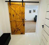 Interiér s posuvnými dřevěnými dveřmi vedoucími do 1-pokojového bytu s podlahou s dřevěným dekorem.