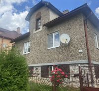 Rodinný dům v Rudné s texturovanou fasádou, zeleným plotem a květinami v zahradě.