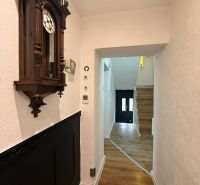 Chodba rodinného domu s hodinami a podlahou s dřevěným dekorem.