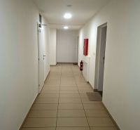 Chodba s bílými stěnami, dlažbou a nouzovým vybavením v garsonce.