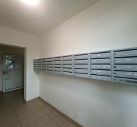 Poštovní schránky ve vstupní hale garsonky, podlaha s dlažbou, jednoduchý design.