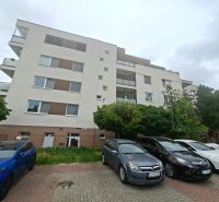 Bytový dům na Športové ulici v Dunajské Lužné s parkovištěm a auty před budovou.
